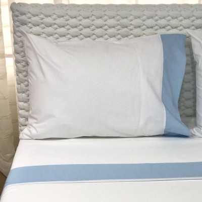Travesseiro branco com faixa azul clara em cama com cabeceira cinza texturizada
