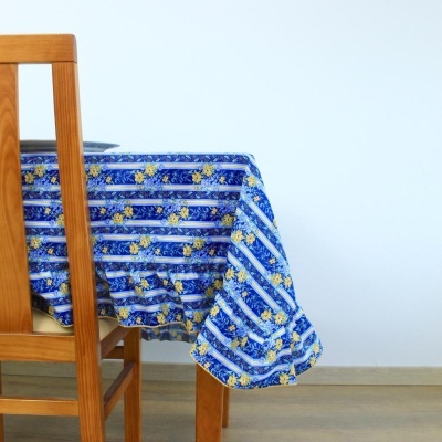 Toalha de mesa azul com flores amarelas e listas brancas sobre mesa de madeira e cadeira ao lado