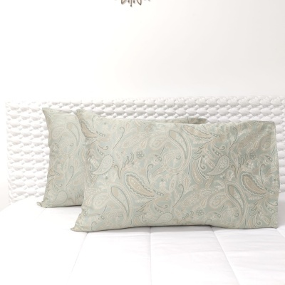 Almofadas retangulares com padrão floral em tons verdes e bege sobre cama branca com cabeceira texturada