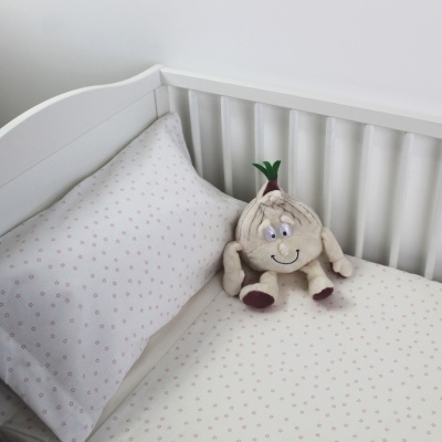Berço branco com roupa de cama branca com padrão rosa e peluche de cabeça de alho