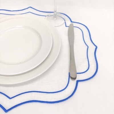 Jogo de jantar com pratos brancos, faca de metal e guardanapo branco com bordado azul