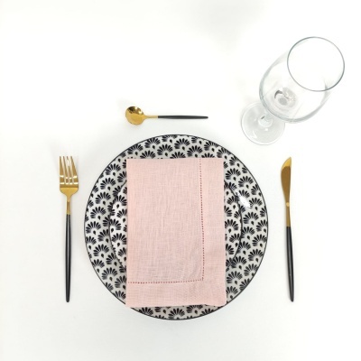 Conjunto de mesa com prato branco e preto, guardanapo rosa, talheres pretos e dourados e copo de vidro