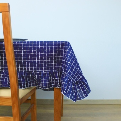 Toalha de mesa azul com padrão de grades brancas numa mesa de madeira clara com cadeira em madeira e parede branca