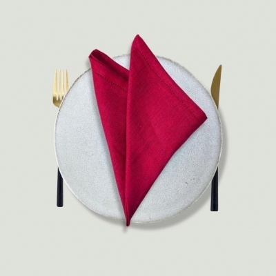 Prato branco com textura, guardanapo vermelho dobrado, garfo e faca dourados com cabos pretos