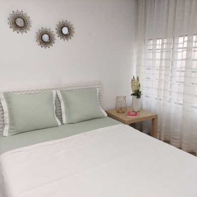 Quarto com cama arrumada, almofadas cinza-verde e mesa de cabeceira com decoração