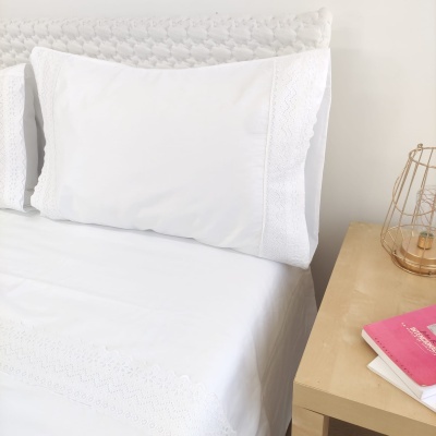 Almofada branca com renda na cama junto a mesa de cabeceira em madeira clara