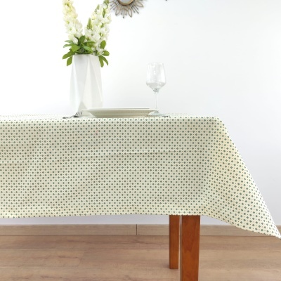 Toalha de mesa branca com padrão de pontos pretos e verdes numa mesa de madeira com prato, copo e vaso com flores brancas