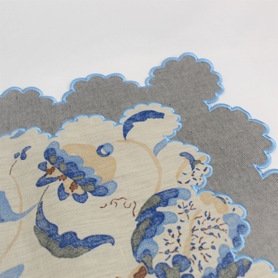 Pano decorativo com padrão floral azul e bege em fundo cinza com bordas onduladas azuis