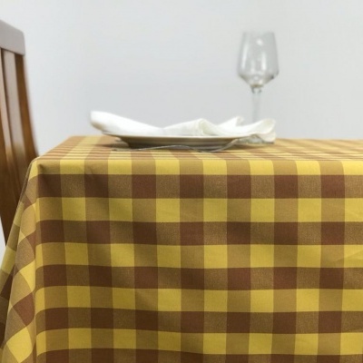 Toalha de mesa xadrez amarelo e castanho sobre mesa de madeira com prato, guardanapo e copo