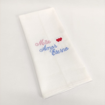 Pano de cozinha branco com bordado colorido 'Mãe Amor Eterno' e dois corações vermelhos.