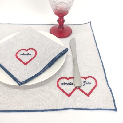 Conjunto de mesa com toalhete e guardanapo bordados com corações e nomes Amélia e José, copo rosa e prato branco