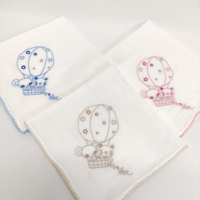 Três panos brancos com bordados de balão de ar quente em azul, rosa e bege