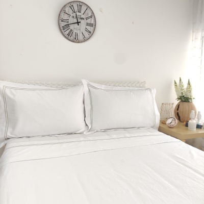 Cama com roupa de cama branca e relógio de parede acima em quarto minimalista