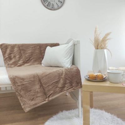 Cobertor castanho sobre sofá branco com almofada, mesa com vaso, doces e chávena