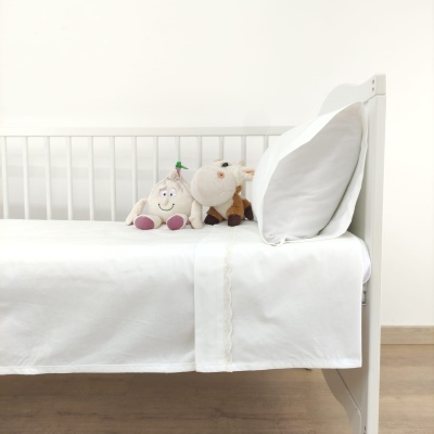 Cama branca com lençol branco e dois peluches, boneco e vaca.