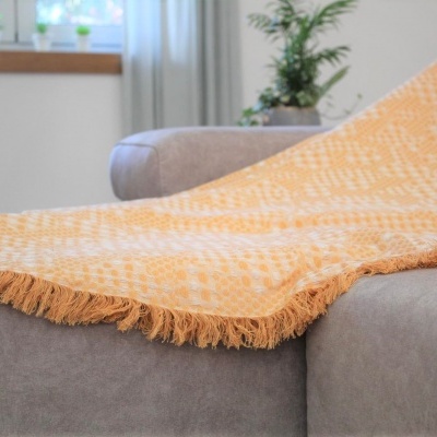 Cobertor amarelo e branco com franjas no sofá cinzento