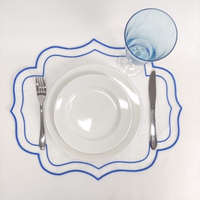 Conjunto de prato branco, copo azul, talheres e jogo americano com borda azul sobre fundo branco