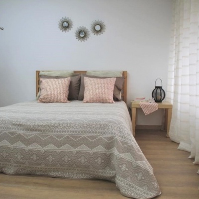 Quarto com cama de casal com colcha bege e decoração minimalista