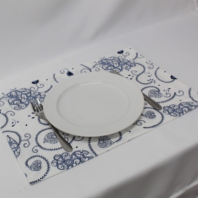 Mesa com toalha branca, individual azul e branco, prato branco e talheres de metal