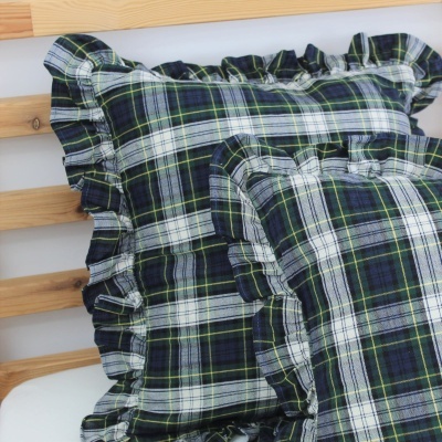 Almofadas xadrez com bordas franzidas sobre superfície branca e estrutura de madeira