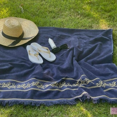 Toalha de praia azul escura com bordado dourado e acessórios de verão sobre relva