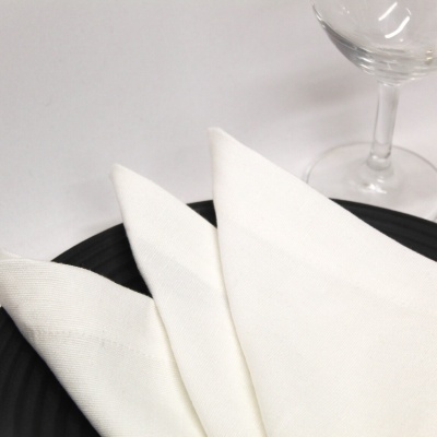 Guardanapo branco dobrado em prato preto com copo de vidro