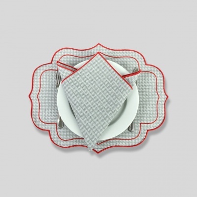 Conjunto de passatempo e guardanapo cinzento com padrão e bordas vermelhas sobre prato branco.