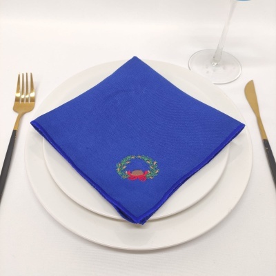 Guardanapo azul bordado sobre pratos brancos com talheres dourados e copo de vidro