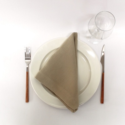 Conjunto de mesa com prato branco, guardanapo bege, talheres com cabo de madeira e copo de vidro