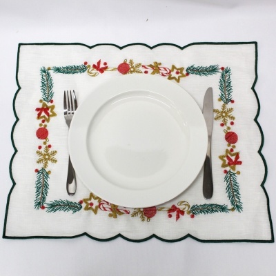 Conjunto de loiça com prato branco e talheres sobre pega de mesa decorada com motivos natalícios bordados