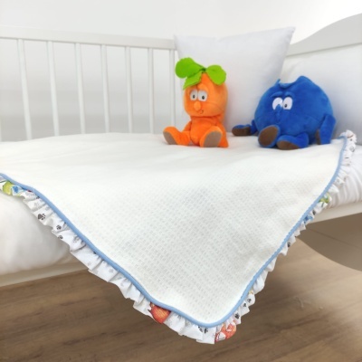 Cobertor branco com babados coloridos sobre cama branca com peluches laranja e azul