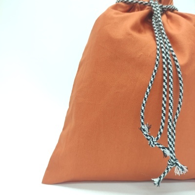 Saco de tecido cor de ferrugem com cordão preto e branco para fecho