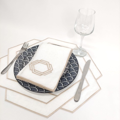 Mesa posta com prato azul e branco, guardanapo branco com detalhe dourado e talheres metálicos ao lado, copo de vidro