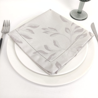 Guardanapo branco com padrão floral cinza sobre prato branco, talheres e copo de vidro cinzento