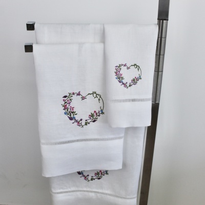 Três toalhas brancas com bordado em forma de coração floral penduradas em suporte metálico
