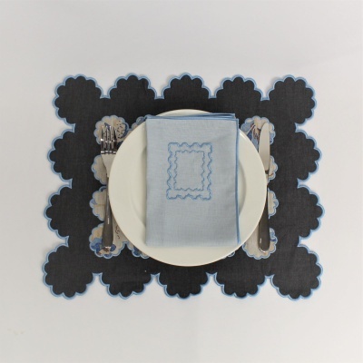 Conjunto de loiça com prato branco, guardanapo azul bordado, talheres e individual preto floral