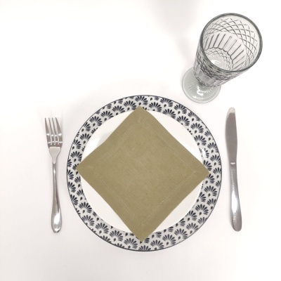 Conjunto de jantar com prato branco decorado, guardanapo verde, talheres prateados e copo de vidro