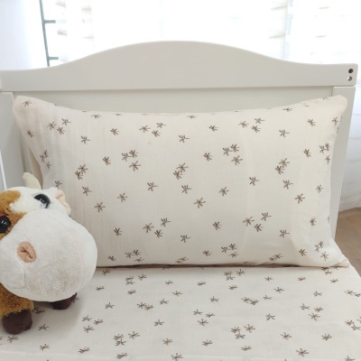 Fronha e lençol brancos com padrão de insetos castanhos junto a peluche de vaca numa cama branca