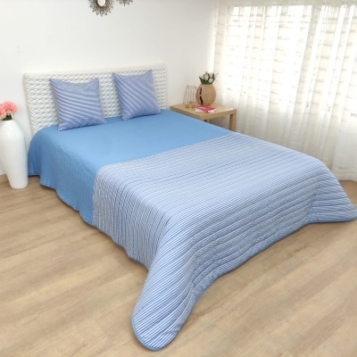 Cama com colcha azul claro e duas almofadas azuis em quarto com luz natural