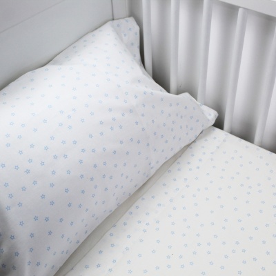 Almofada e lençol branco com padrão de estrelas azuis numa cama com cabeceira branca.