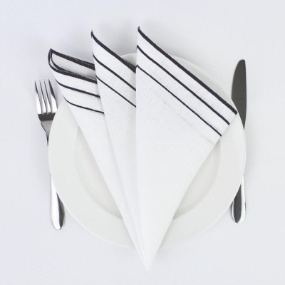 Guardanapos brancos com riscas pretas sobre prato branco com talheres al lado.
