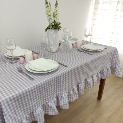 Mesa posta com toalha de mesa xadrez lilás e branca com babados, pratos, copos, velas e jarro com flores