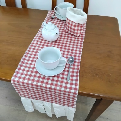 Mesa de madeira com caminho de mesa xadrez vermelho e branco, conjunto de chá branco e cesto com guardanapos.