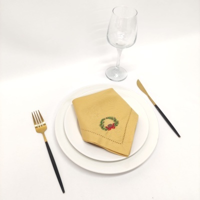 Jogo de jantar com pratos brancos, guardanapo amarelo bordado, talheres dourados e pretos, copo de vidro.