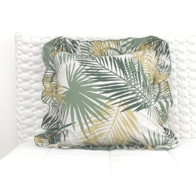 Almofada com padrão de folhas verde e bege sobre sofá branco acolchoado