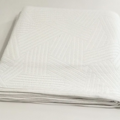 Lençol branco dobrado com padrão geométrico em relevo sobre superfície branca