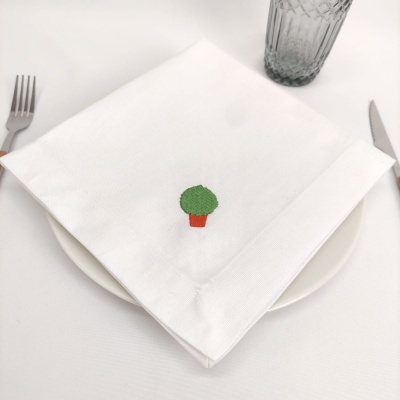 Guardanapo branco com bordado de planta em mesa com prato, talheres e copo