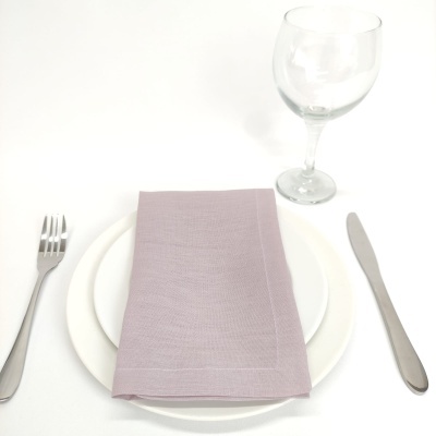 Conjunto de pratos, guardanapo lilás, talheres metálicos e copo de vidro sobre fundo branco