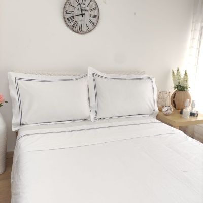 Cama arrumada com roupa de cama branca com linhas pretas e decoração de quarto com relógio e mesa de cabeceira.