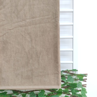 Toalha de banho bege pendurada em estrutura branca com folhas verdes